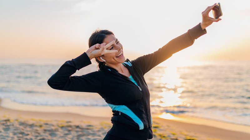 young-smiling-attractive-slim-woman-doing-sport-exercises-morning-sunrise-beach-sports-wear-healthy-lifestyle-listening-music-earphones-making-sel